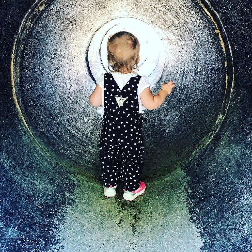 A toddler in heart-print overalls standing in the tunnel at Underwood Family Farms, 2018